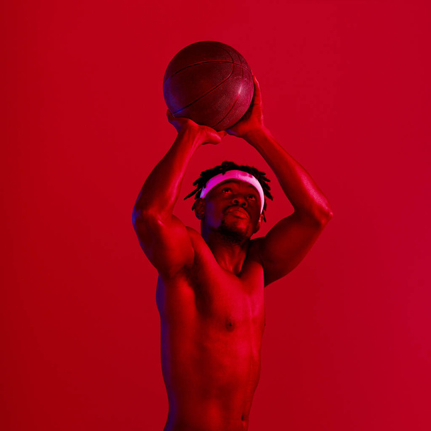 撃たれてるぞ。スタジオでバスケットボールをしている若いスポーツマンの赤いフィルターショット. - 写真・画像