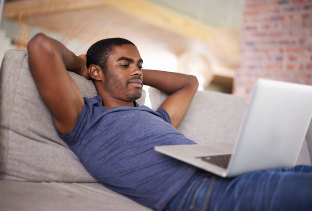 Relaxar com o mundo inteiro ao meu alcance. Tiro cortado de um jovem bonito usando seu laptop enquanto relaxa em casa. - Foto, Imagem