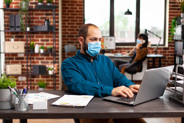 Bookkeeper hombre con protección máscara facial médica contra covid19 sentado en el escritorio - Foto, Imagen