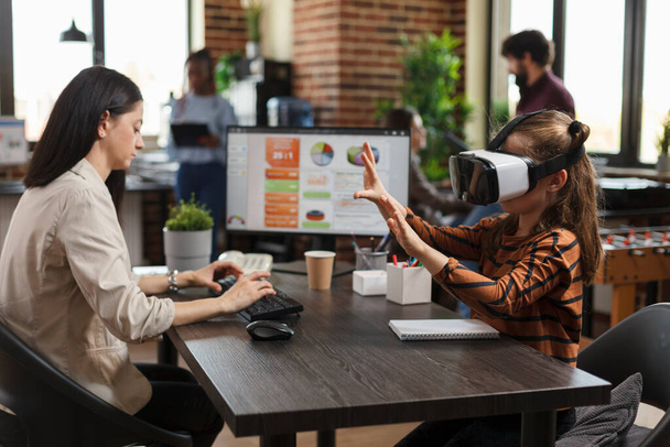 Játékos kisgyerek visel VR headset élvezi a virtuális valóság technológia, miközben elfoglalt anya dolgozik a számítógép. - Fotó, kép