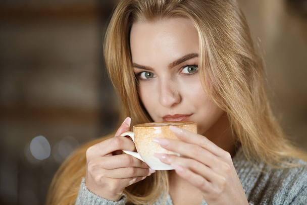 Portrait of a young beautiful woman sitting in modern cafe bar interior having a cup of coffee - Photo, image