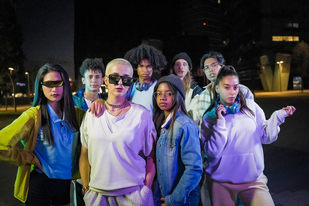 Group of young people with modern outfits in the street wth neon lights at night looking to the camera. - Foto, immagini