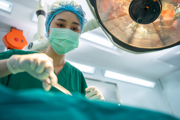 Команда азиатских профессиональных хирургов, выполняющих хирургические операции в операционной, хирургов, ассистентов и медсестер - Фото, изображение