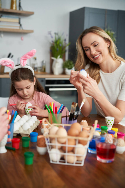 Cheerful caucasian mother and daughter decorate easter eggs at home - Photo, Image