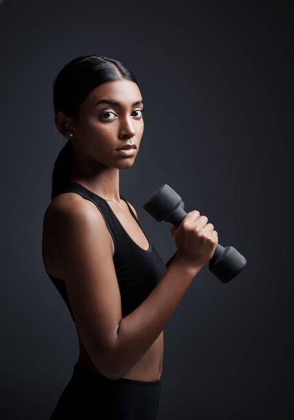 Two of the most intimidating traits are strength and beauty. Studio portrait of a young sportswoman doing dumbbell exercises against a gray background. - Photo, image