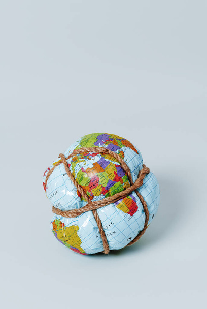un globe terrestre étroitement attaché avec une corde sur un fond bleu pâle, avec un peu d'espace vide sur le dessus - Photo, image