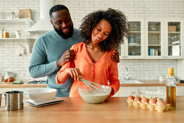 Cute African American para przygotować słodkie ciasta na śniadanie i spędzić romantyczny czas razem w kuchni w domu. - Zdjęcie, obraz