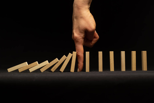 Megállítani egy lezuhanó dominót az ujjaddal. A válságkezelés fogalma, a kockázat. Vezetői készségek. - Fotó, kép