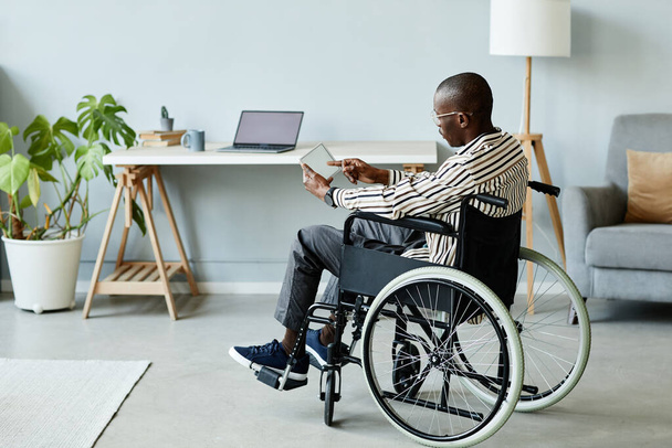 Retrato de comprimento total do homem afro-americano em cadeira de rodas usando tablet com tela em branco no interior da casa mínima, espaço de cópia - Foto, Imagem