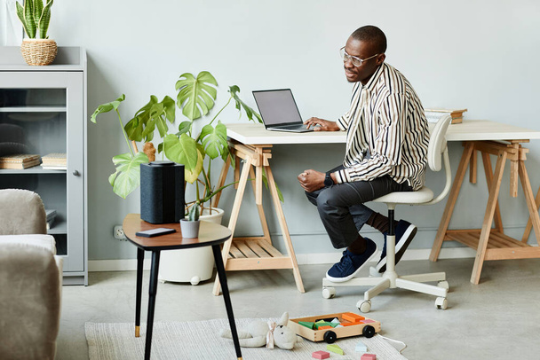 Full length portrait of African American man using voice activated smart speaker in minimal home interior, copy space - Foto, imagen