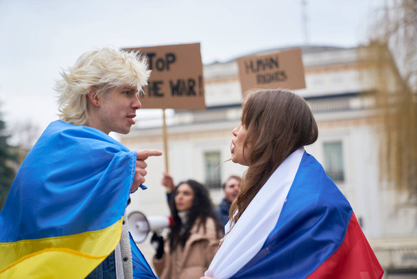 Кавказька жінка з російським прапором сперечається з кавказьким чоловіком з українським прапором на вулиці.  - Фото, зображення