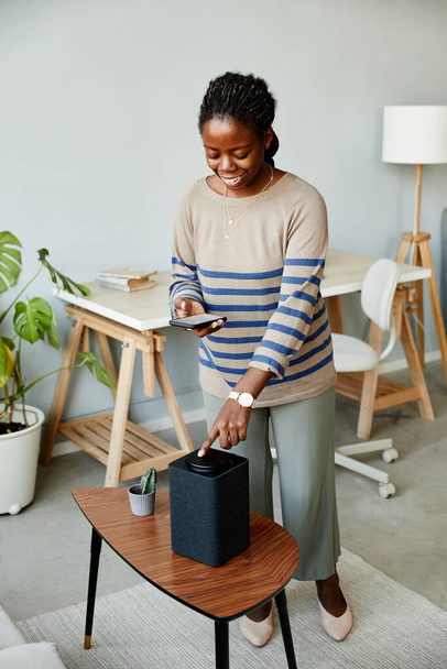Vertical portrait of smiling African American woman using voice activated smart speaker in modern home - Fotografie, Obrázek