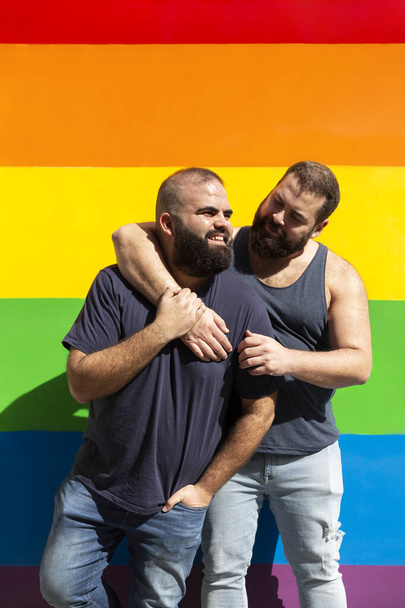 Joven pareja gay abrazándose sobre un fondo con colores arcoíris. Concepto de orgullo LGBT. - Foto, Imagen