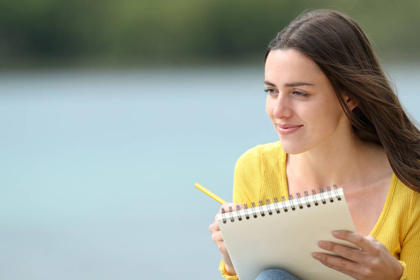 Satisfied woman drawing on notebook sitting in a lake - Foto, imagen