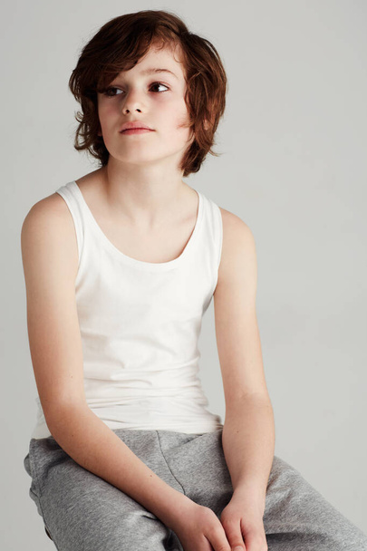 Candid and casual. A young boy sitting on a stool in the studio while looking away. - Fotoğraf, Görsel
