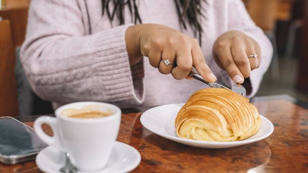 afro vrouw met een Frans ontbijt met koffie en croissant zittend in het café - Foto, afbeelding