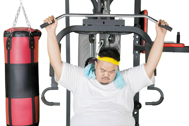 Image of fat man looks tired while exercising with weightlifting machine in the studio. Isolated on white background - Fotoğraf, Görsel