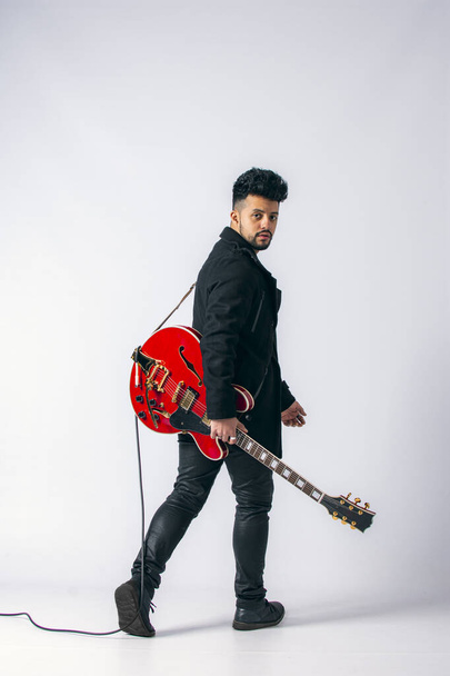 Esmer, siyah saçlı ve sakallı, beyaz arka planda kırmızı elektro gitar çalan Latin bir adamın stüdyo fotoğrafı.. - Fotoğraf, Görsel