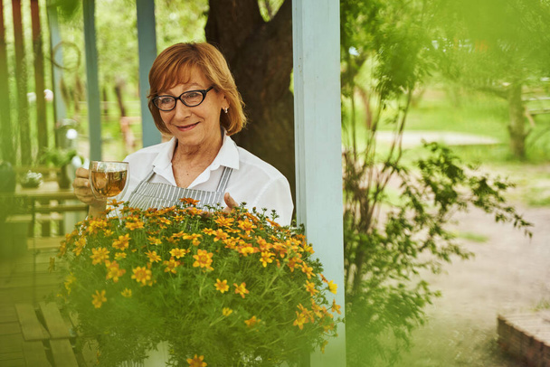 Happy aged woman enjoying tea on blooming terrace - Foto, Bild