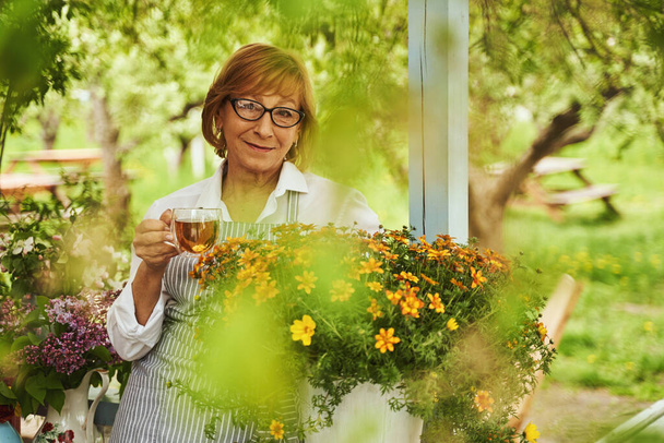 Smiling bespectacled lady with cup of tea on terrace - Fotó, kép