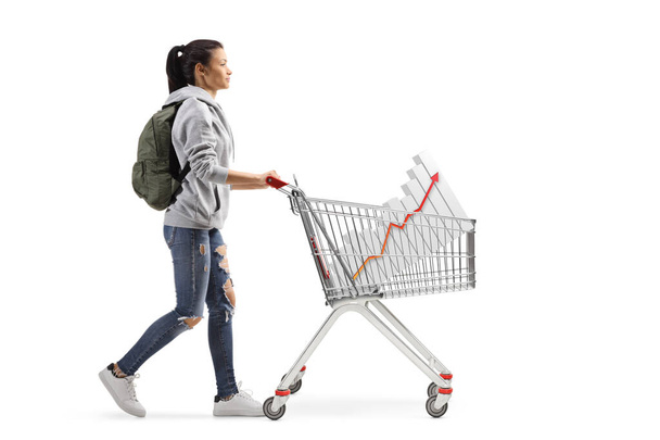 Full length profile shot of a female student walking and pushing a shopping cart with a bar chart isolated on white background - Foto, immagini