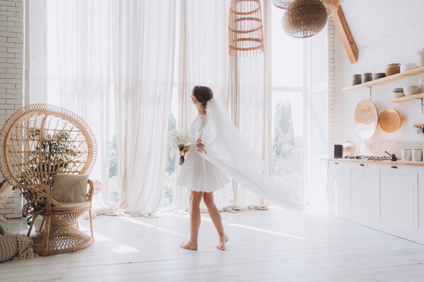Morning of the bride in a rustic style, in a white bathrobe and a white bouquet on the bed and in the bathroom by the window in a photo studio, in a hotel - Photo, image