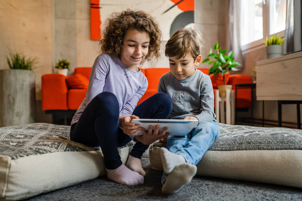 Siblings brother and sister boy and girl or children friends using digital tablet at home i room to watch video make a call or play online games leisure family concept real people copy space - Photo, Image