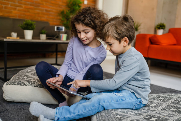 Siblings brother and sister boy and girl or children friends using digital tablet at home i room to watch video make a call or play online games leisure family concept real people copy space - Photo, Image