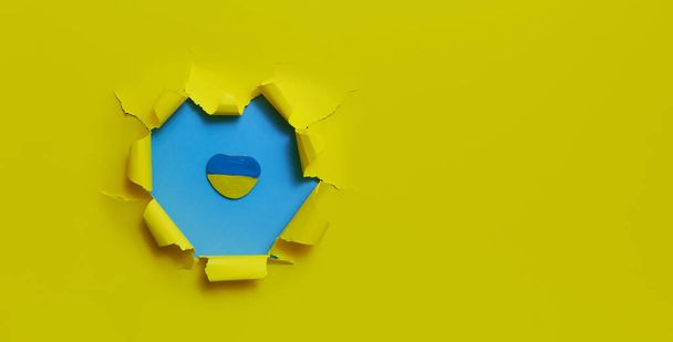 A stone in the shape of a heart is painted in the colors of the Ukrainian flag. A hole in yellow against a blue background from a military shell. Conflict in Ukraine. War in Ukraine 2022.  - 写真・画像