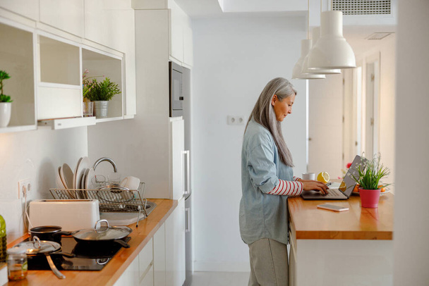 Donna che utilizza il computer portatile in cucina in appartamento moderno - Foto, immagini