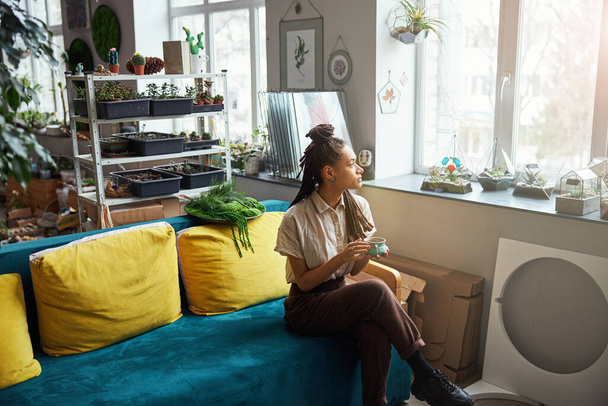 Pensive beautiful florist with cornrows looking out of the window - Fotoğraf, Görsel