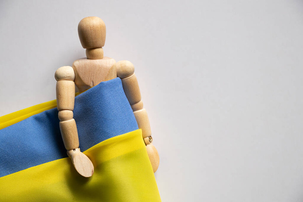 Желто-голубой национальный флаг Украины и деревянный человек на белом фоне, остановить войну и мир на Украине 2022 - Фото, изображение