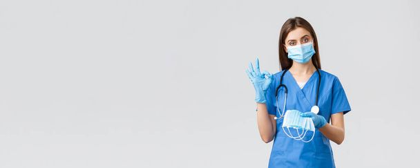 Ковід-19, запобігання вірусу, здоров'ю, концепції працівників охорони здоров'я. Професійна медсестра або лікарка в блакитних скрабах і засобах індивідуального захисту, показують добре знак і дають медичну маску
 - Фото, зображення