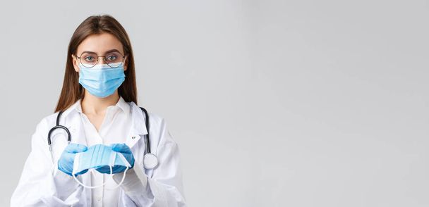 Covid-19, het voorkomen van virus, kliniek, gezondheidswerkers en quarantaine concept. Jonge arts in medisch masker en handschoenen, witte scrubs, het geven van gezichtsmasker bescherming aan patiënten, kijk ernstig - Foto, afbeelding