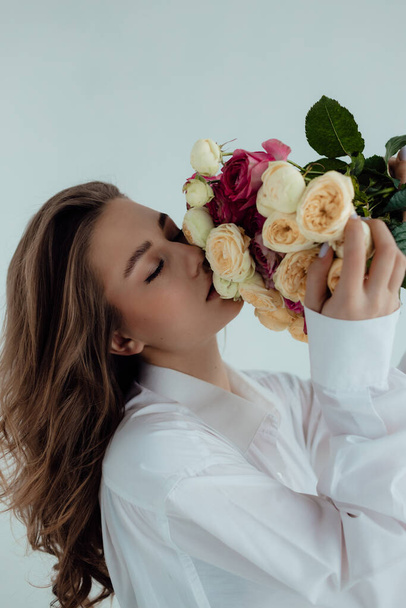 Piękna modelka z bukietem róż. Wiosenna dama na jasnym tle. Kobiece ciało i koncepcja stylu. Reklama lub projekt wyprzedaży ubrań. Przestrzeń tekstu - Zdjęcie, obraz