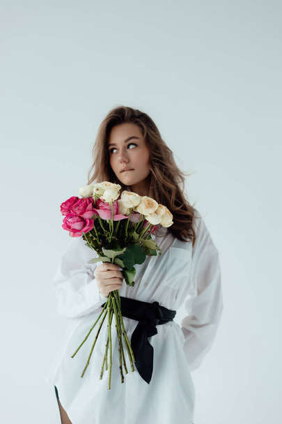 Beautiful girl model with a bouquet of roses. Spring Lady on light background. Female body and style concept. Advertisement or clothes sale design. Space of text - Photo, Image