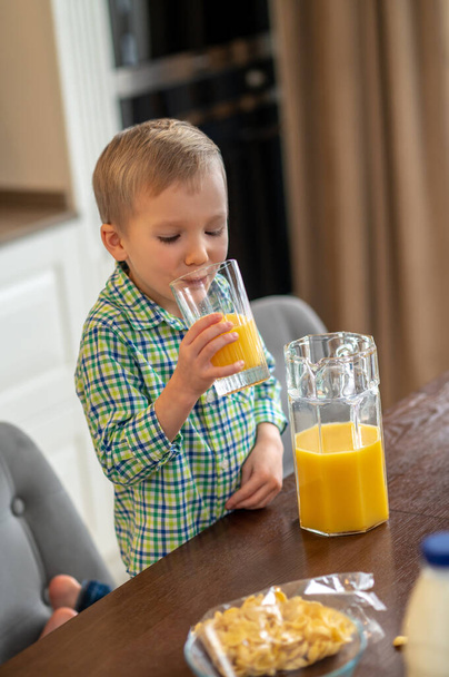 Calm little boy sipping orange juice indoors - Foto, imagen