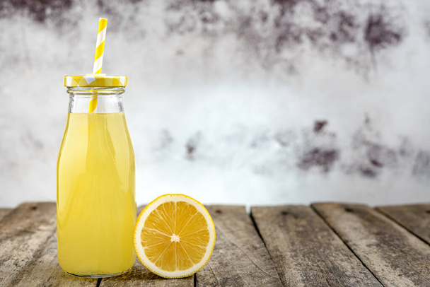 Fles koude limonade met stro en citroenschijfje op rustieke houten tafel. - Foto, afbeelding
