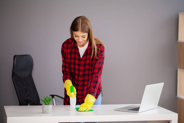 Junge Arbeiterin putzt Schreibtisch mit Lappen im Büro - Foto, Bild