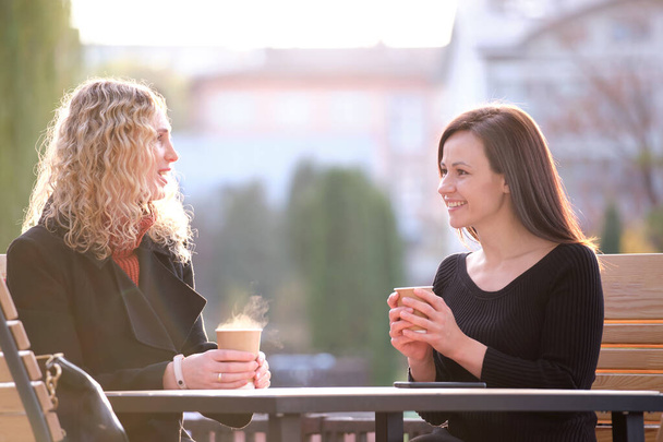 Portret van twee gelukkige jonge vrouwen zittend in City Street Café - Foto, afbeelding