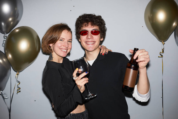 Vita in su ritratto di sorridente giovane coppia festa e guardando fotocamera che tiene bevande, girato con flash - Foto, immagini