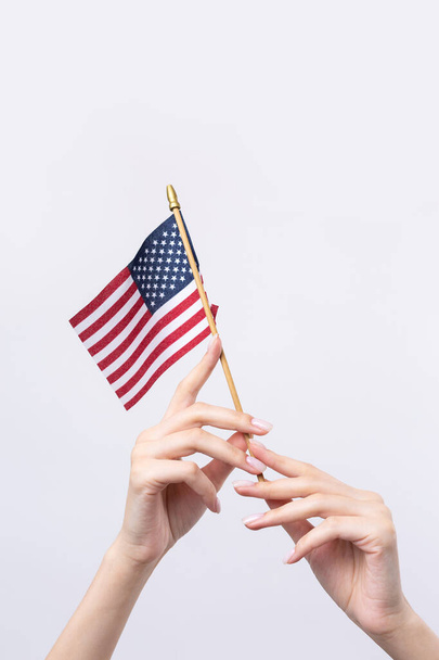 A beautiful female hand holds an American flag on a white background. - Zdjęcie, obraz