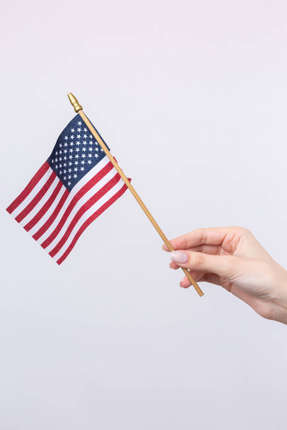 Una bella mano femminile tiene una bandiera americana su sfondo bianco. - Foto, immagini