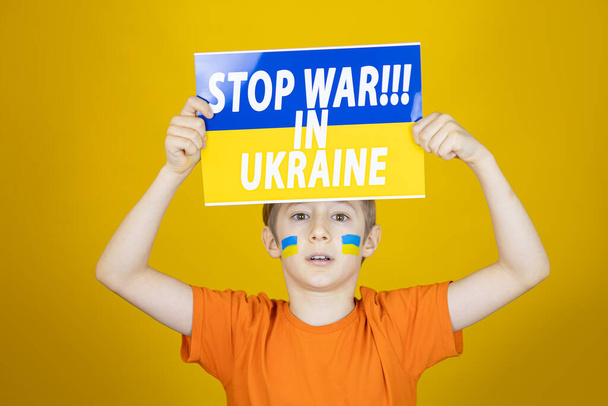 un niño triste levantó un cartel con la inscripción detener la guerra en Ucrania - Foto, imagen