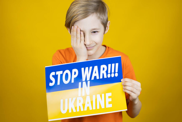 smutny chłopiec z plakatem w ręku z napisem zatrzymać wojnę na Ukrainie pochylił rękę do głowy - Zdjęcie, obraz