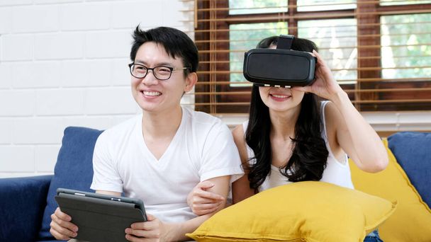 Щаслива азіатська пара грає в імітацію віртуальної реальності, сидячи на дивані в домашній вітальні, люди і технології
 - Фото, зображення