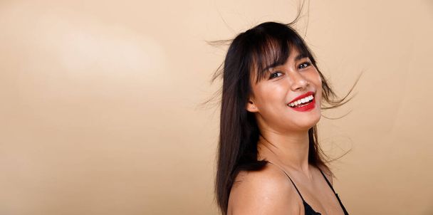 Asiatisch indisch-arabische Mischlingshündin 20er Jahre lächelt glücklich, als sie mit hochgeschminkten schwarzen kurzen Haaren posiert. Weibliches Gesicht aus nächster Nähe über gelb-beigem Hintergrund aufgenommen  - Foto, Bild
