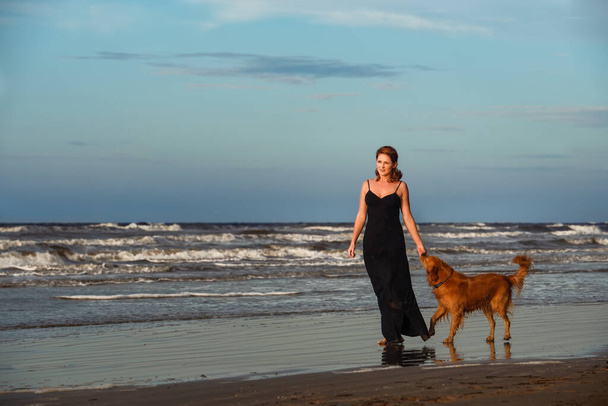 smiling young woman playing with her dog on the beach - Foto, imagen