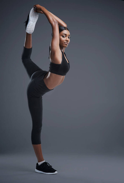 So heftig sie auch ist, sie ist flexibel. Studioporträt einer sportlichen jungen Frau, die ihren Körper vor grauem Hintergrund streckt. - Foto, Bild