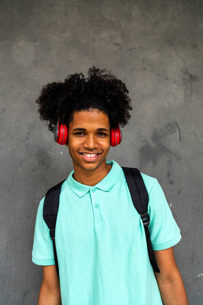 Pionowy portret szczęśliwego nastolatka Afroamerykanin chłopiec z afro fryzura patrząc na aparat noszący słuchawki. - Zdjęcie, obraz